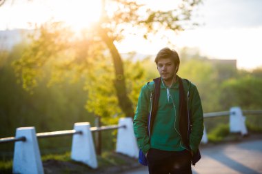 Gün batımında kulak içi kulaklık ile müzik dinlemek şehirde yürüyüş ortak genç adam. Yumuşak sıcak ışık.