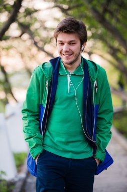 gülümseyen ve müzik Park şehir etrafında yürüyen yakışıklı adam. Yumuşak günbatımı ışığı.