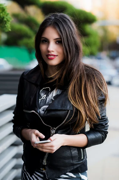 Chica caminando y mensajes de texto en el teléfono inteligente en la calle con una chaqueta de cuero en verano — Foto de Stock