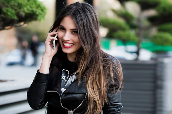 Retrato de sonriente hermosa mujer joven de cerca con teléfono móvil, contra el fondo de la calle verde de verano — Foto de Stock