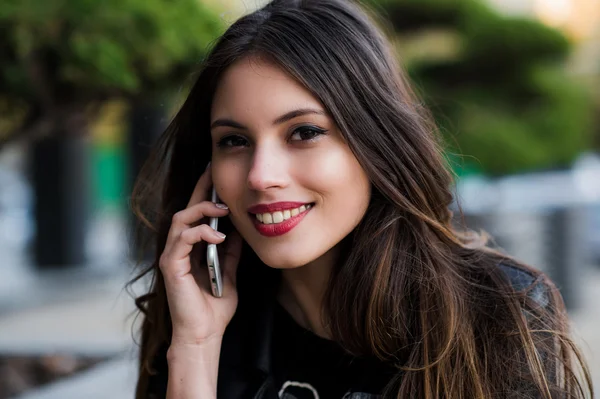 Retrato de una hermosa mujer con una sonrisa blanca perfecta hablando en el teléfono móvil al aire libre — Foto de Stock