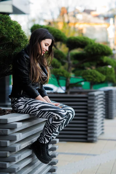 Jeune belle femme tenant le téléphone portable dans la main et assis sur le banc dans le parc de la ville — Photo