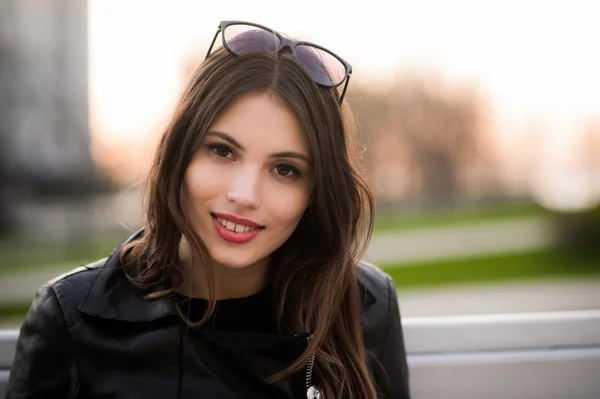 Retrato cercano de una hermosa joven morena sonriente, contra el parque verde de verano al atardecer — Foto de Stock