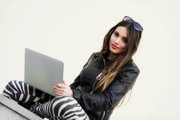 Die schöne Studentin lächelt mit einem Laptop und sitzt auf einer alten Mauer auf dem Campus der Universität. wunderschönes Mädchen, das im College-Park mit dem Computer arbeitet. — Stockfoto