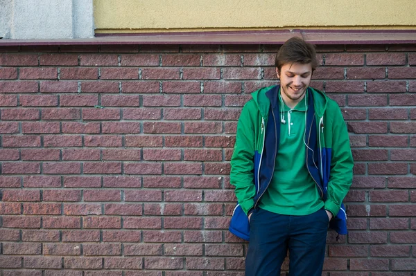 Gewone jonge man dragen groene t-shirt jas en jeans tegen een rode bakstenen muur op zoek naar de camera — Stockfoto