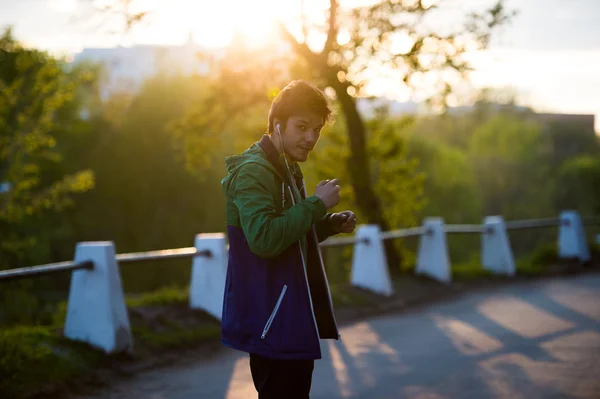 常见的年轻人，行走在城市在日落的时候听听音乐与入耳式耳机。柔软温暖的光. — 图库照片