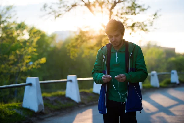 Tonas foto av gemensamma ensam ung promenader i staden lyssna på musik med in-ear hörlurar i solnedgången. Mjuka varma ljus. — Stockfoto