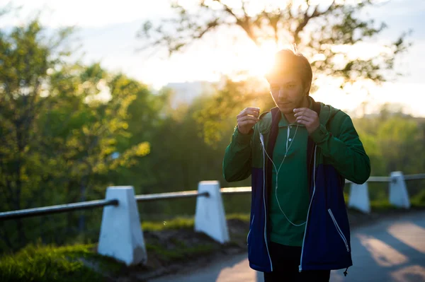 Звичайний молодий чоловік ходить по місту слухаючи музику з навушниками на заході сонця. М'яке тепле світло . — стокове фото