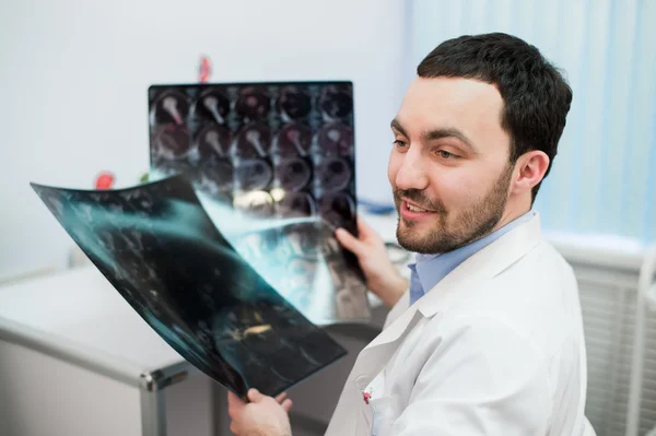 Ο γιατρός νοσοκομείο κρατώντας ασθενείς φιλμ ακτίνων χ και η μαγνητική τομογραφία, κοιτάζοντας μακριά χαμογελώντας — Φωτογραφία Αρχείου
