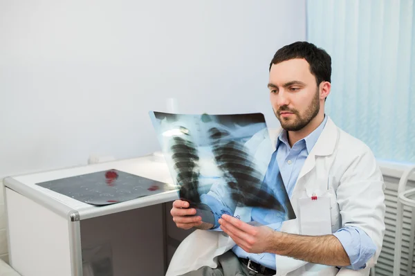 Health and mood. Serious Doctor talking to patient keeps chest X-ray in hands while sitting at a table the hospital.