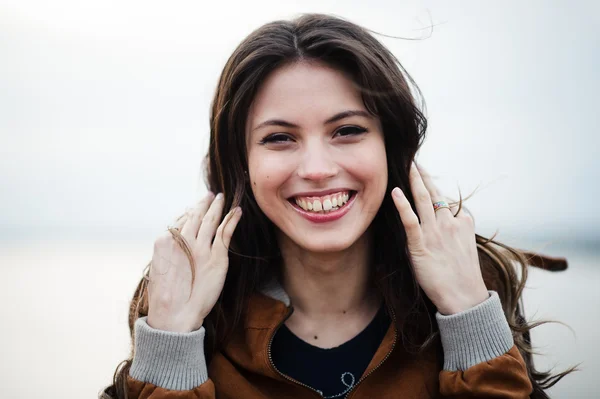 Primer plano retrato de joven feliz hermosa mujer atractiva con abrigo de cuero sonriendo y de pie sobre la luz al aire libre fondo . — Foto de Stock
