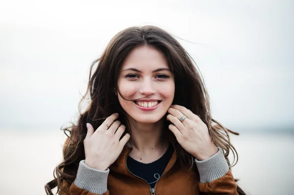 Primer plano retrato de joven feliz hermosa mujer atractiva con abrigo de cuero sonriendo y de pie sobre la luz al aire libre fondo . — Foto de Stock