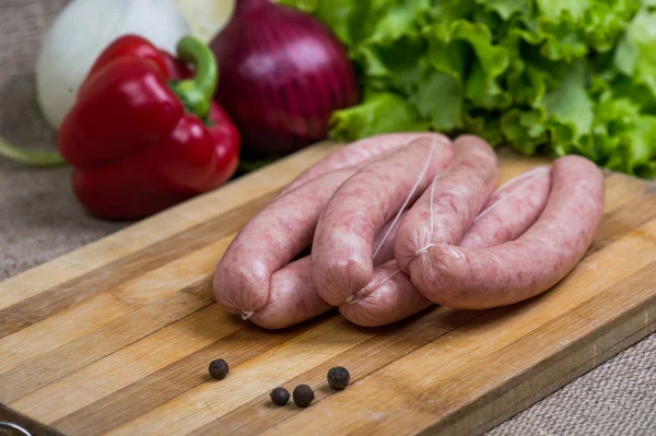 Сырые колбасы с овощами на деревянной доске — стоковое фото