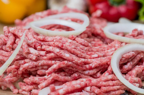Сырое мясо и луковые кольца крупным планом со свежими овощами на заднем плане — стоковое фото