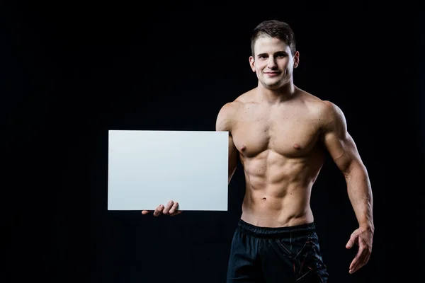 Bodybuilder complet du corps avec affiche blanche vierge isolé sur fond noir. bel homme musclé tenant copyspace tableau gris dans les mains . — Photo