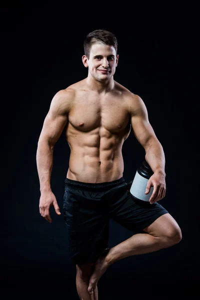 Bodybuilding und Sport Thema: schöner kräftiger Bodybuilder, der im Studio ein Plastikgefäß mit trockenem Protein hält, das sich entspannt isoliert auf schwarzem Hintergrund anfühlt — Stockfoto