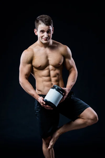 Bodybuilding e Sport tema: bel bodybuilder forte in possesso di vaso di plastica con una sensazione di proteine secche rilassato isolato su sfondo nero in studio — Foto Stock