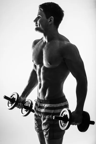 Unga och passform manlig modell poserar hans muskler pumpar upp med hantlar i ett gym ute till vänster isolerad på vit bakgrund. — Stockfoto