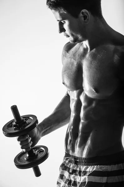 Close up of muscular bodybuilder guy doing exercises with weights dumbbell over isolated light background. Black and white — Stock Photo, Image