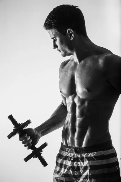 Mladí a fit mužský model, představují jeho svaly se čerpání s činkami v tělocvičně dívajícího se doleva, izolované na bílém pozadí. — Stock fotografie