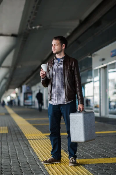 Молодой привлекательный мужчина пьет кофе по пути к терминалу аэропорта, глядя в камеру — стоковое фото