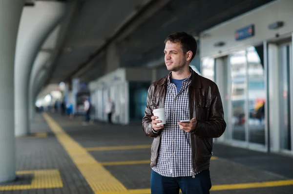 Человек с сотовым телефоном и чашкой кофе возле терминала аэропорта — стоковое фото