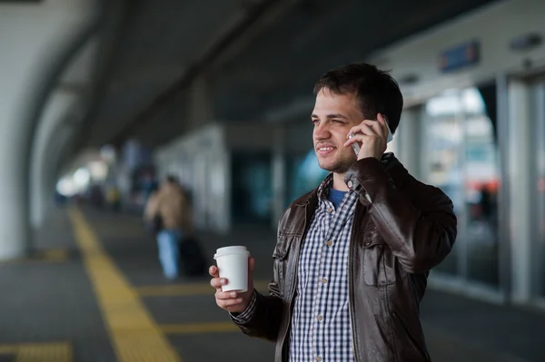 Man Using Mobile Phone near the airport terminal with a cup of coffee waiting for the taxi — Stock Photo, Image