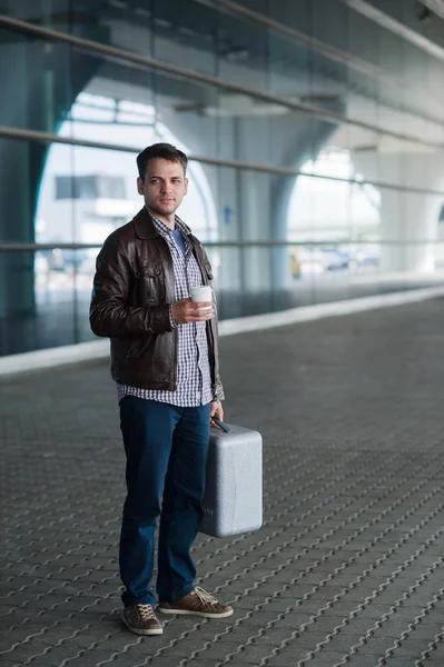 Full längd porträtt unga glada leende stilig resande mannen i 20-talet lämnar ankomster flygplatser lounge terminal byggnaden efter att samla in sitt bagage med en kopp nybryggt kaffe — Stockfoto