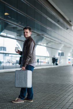 Havaalanı terminal yakınındaki bavul ve kahve Kupası ile yürüyen bir genç adam profil portresi