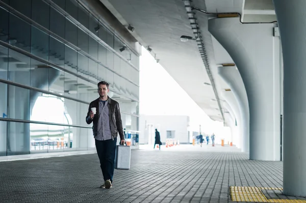 空港ターミナルのそばのスーツケースとコーヒー カップと歩いて若い男の横顔の肖像画 — ストック写真