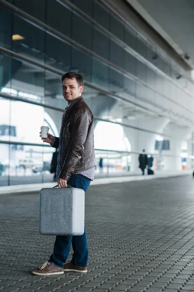 Profil porträtt av en ung man promenader med resväska och kaffe kopp nära flygplatsterminalen — Stockfoto