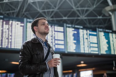 Havaalanı yakınlarında uçuş takvim kahve tutan bir torba ile genç adam