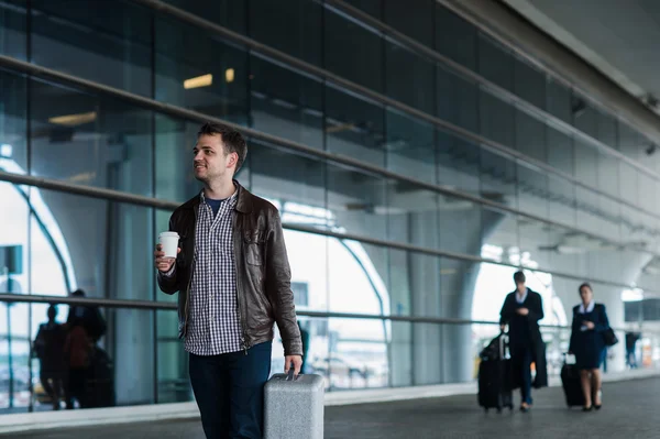 Портрет молодого человека, идущего рядом с аэропортом с чемоданом и кофе — стоковое фото