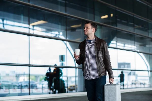 Retrato de um jovem caminhando perto do aeroporto com mala e café — Fotografia de Stock