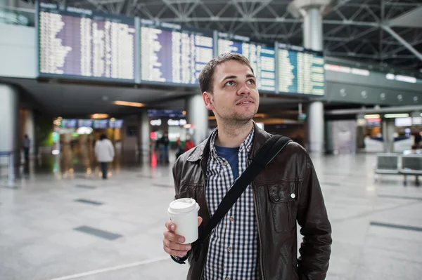 Nachdenklich lächelnder Mann vor der Ankunfts- und Abflugtafel am Flughafen bei einem Kaffee — Stockfoto
