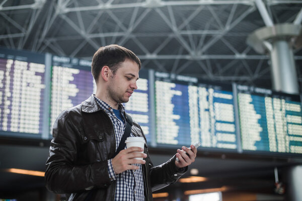 Cheerful man with coffee on the mobile phone in front of Board schedules in airport terminal