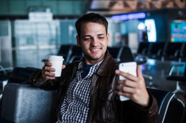 Gülen ve selfie kahve ile havaalanında uçağı bekleyen alarak genç bir adam portresi