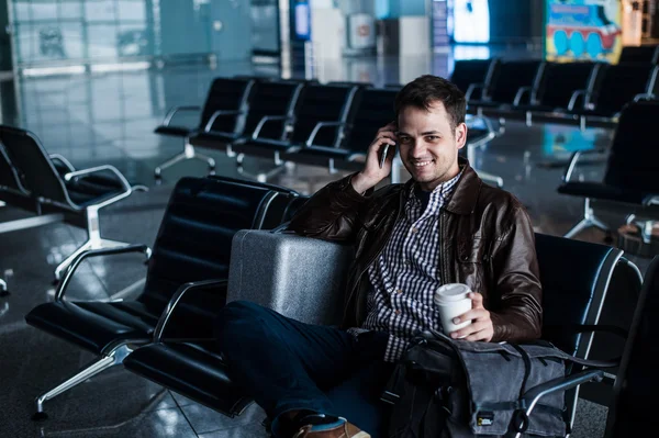 Stilig ung man med svart hår arbetar, sitter på en stol saker på flygplatsen väntar på sin flight — Stockfoto