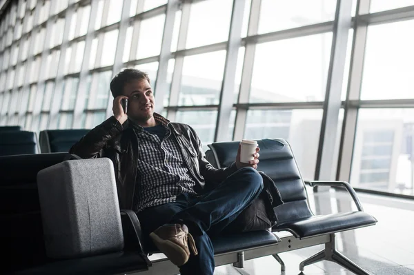 Joven guapo con el pelo negro trabajando, sentado en una silla cosas en el aeropuerto esperando su vuelo —  Fotos de Stock