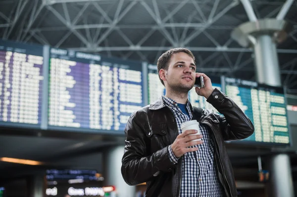 Leende ung resande man på flygplatsen prata telefon framför tidsplan styrelse — Stockfoto