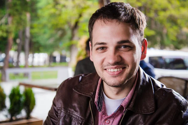 En ung, voksen mann som sitter på kafe eller gatekjøkken og smiler – stockfoto