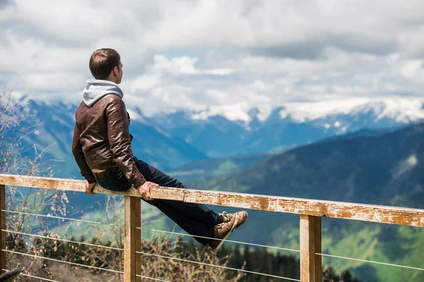 Ο άνθρωπος που κάθεται στο ξύλινο κιγκλίδωμα ψάχνει στην προβολή βουνά και χαλάρωση — Φωτογραφία Αρχείου