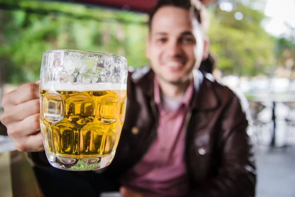 Closeup portrait of handsome guy drinking his beverage at outside cafe veranda. Selective focus on beer.