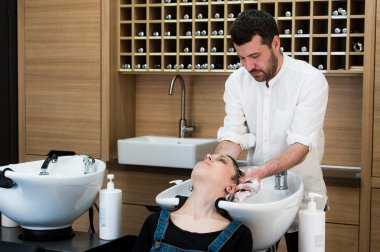 Hairstylist washing head to the young woman at the hairdresser clipart