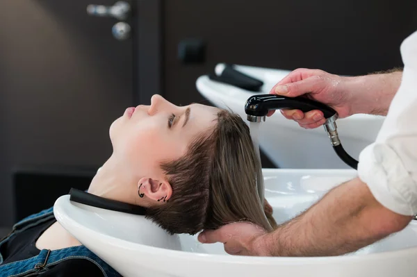 Young teenager girl in hairdressing salon washing hair by male hairdressers hands. — Stock Photo, Image