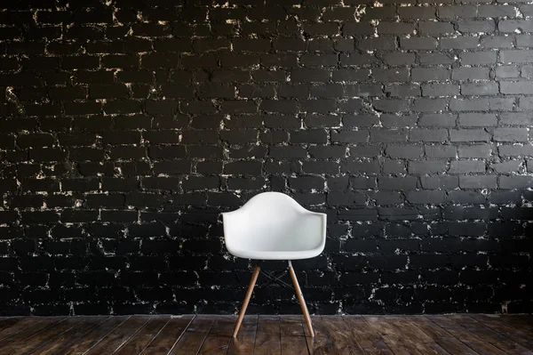 Chaise blanche debout dans la chambre sur le plancher de bois brun sur le mur de briques noires — Photo