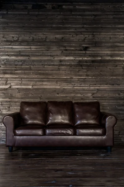 Vintage brown leather sofa on a wooden wall and floor — Stock Photo, Image