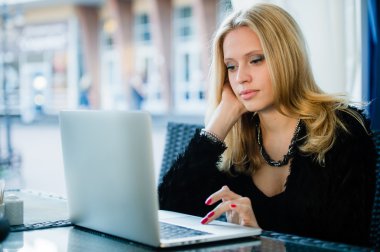 Young gorgeous woman drinking coffee while sitting with open laptop computer outdoors, female freelancer working on notebook in sidewalk cafe, pretty student girl surfing the net outside on terrace clipart