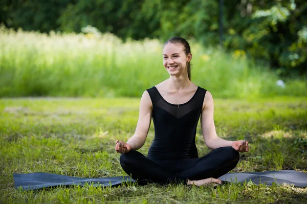 Жінка йога на зеленій траві в позі лотоса посміхається — стокове фото
