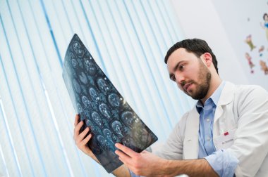 Fikri adam sağlık personel arıyor beyin x-ray radyografik görüntü, ct taraması, MRI, klinik office arka plan beyaz stetoskop ile portre portre. Radyoloji bölümü